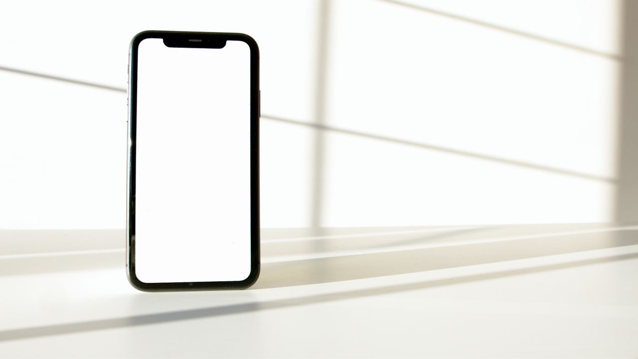 Un smartphone élégant posé sur une surface blanche, avec un contraste marqué entre ombre et lumière.